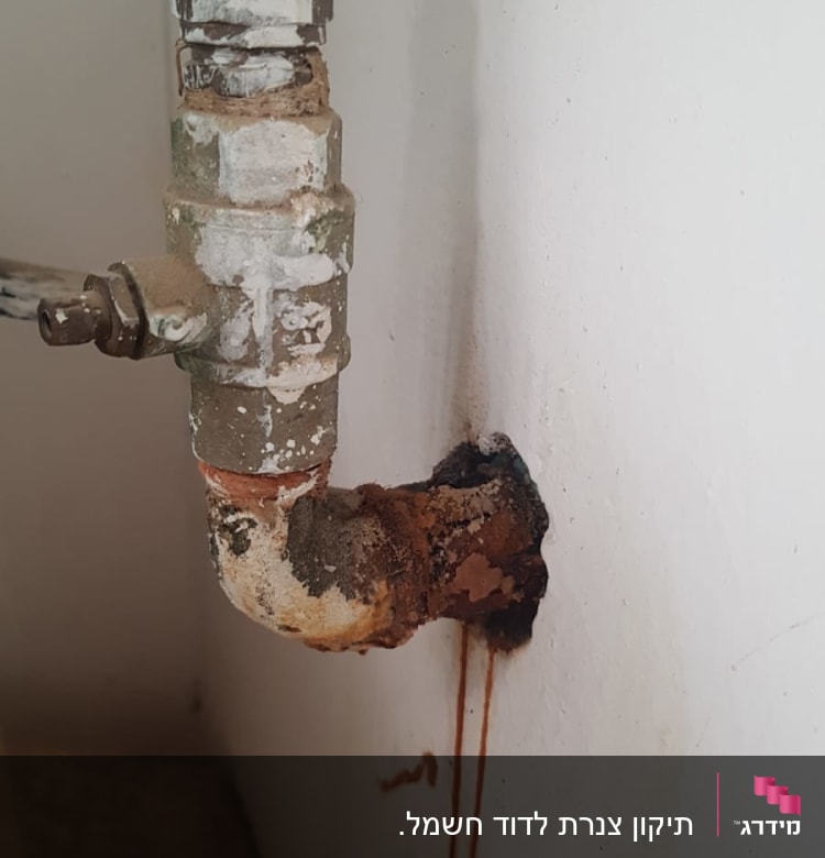 צינור חלוד עם נזילה על קיר לבן